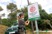 Una agent rural desplegant un cartell que informa sobre el tancament d'un parc natural.