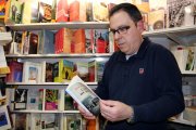 Pla mig d'Octavi Serret, enmig dels llibres del seu establiment de Vall-de-roures, fullejant un exemplar del 'Camí de Sirga' de Jesús Moncada. Imatge del 21 d'abril de 2017 (horitzontal)