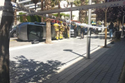 Imatge de la zona acordonada per la Policia Local amb el cotxe bolcat de fons i efectius dels Bombers treballant en el servei.