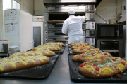 Coques de Sant Joan amb un pastisser obrint el forn en un segon pla a l'obrador.