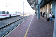 L'estació de l'Aldea-Tortosa-Amposta, amb viatgers a l'andana mentre un tren ràpid passa de llarg sense fer parada.