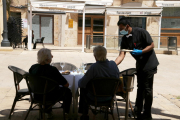 Dos clients d'esquenes i d'un cambrer servint els plats en una terrassa de la plaça de la Font