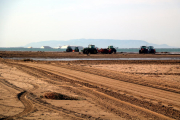 La màquines treballant per donar pas a la barra del Trabucador, amb les instal·lacions de les salines al fons