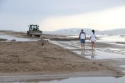 Dues persones i un gos caminant a prop d'una màquina treballant a la barra del Trabucador.