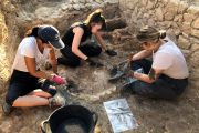 Unes arqueòlogues excavant una llar de foc de l'estança; al fons, l'estructura de la cuina grega del segle VI aC.