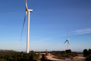 Dos dels grans aerogeneradors del parc la Collada del Perelló amb màquines treballant.