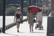 Una dona es protegeix del sol amb un paraigua i una altra amb una gorra, mentre caminen pel pont Vell de Lleida.