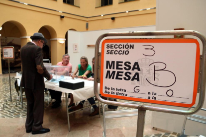Un cartel indicativo y de un elector votando en uno de los colegios electorales de la ciudad de Tarragona.