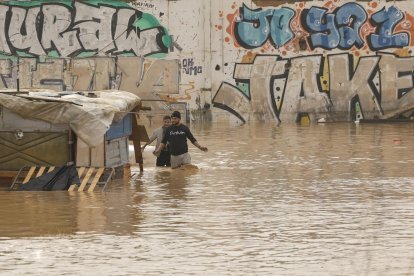 Dos personas vorean un terreno de barracas inundado al lado de la V-30 a causa de las lluvias torrenciales