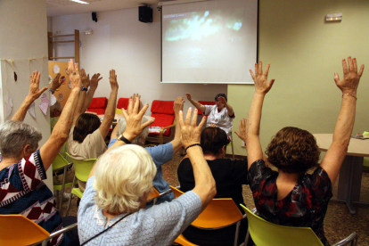 Un grupo de abuelos levantan las manos siguiendo las instrucciones de una terapeuta en un taller de psicomotricidad a la asociación AFAB para enfermos de Alzheimer.