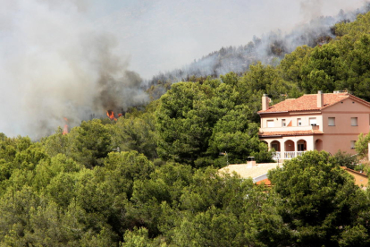 Pla general d'una casa enmig d'una zona boscosa de la Pobla de Montornès, on crema un incendi. Les flames apareixen darrere la finca. Imatge del 5 d'agost de 2016.