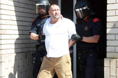 Uno de los detenidos escoltados por dos Mossos D'Esquadra en la salida de uno de los domicilios registrados del barrio del Templo de Tortosa.