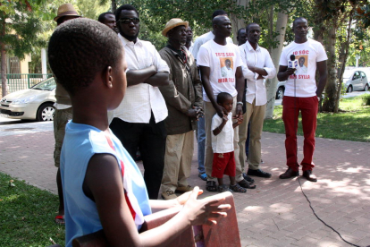 Pla general d'un grup de senegalesos i del germà de Mor Sylla sent entrevistat per una televisió senegalesa, amb un nen en primer terme, d'esquenes, l'11 d'agost a la plaça de la Pau de Salou