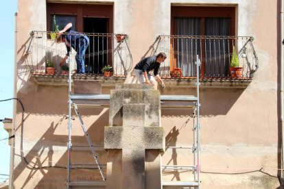 Una veïna al balcó amb les plantes mentre un operari preparava la retirada de la creu franquista de Vilalba dels Arcs, aquest 6 de juny de 2017