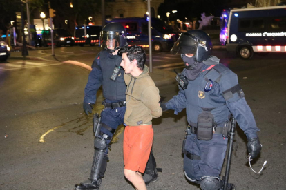 Plano medio de dos agentes y un manifestante detenido en la fuente del Centenari de Tarragona durante los disturbios en la ciudad.