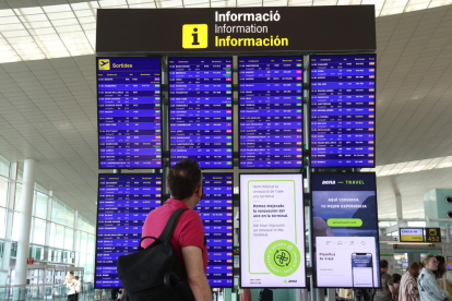 Un passatger mira els panells informatius de la terminal 1 de l'aeroport del Prat.