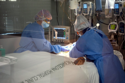 Dues professionals sanitàries de l'Hospital Clínic amb un pacient ingressat a l'Àrea de Vigilància Intensiva (AVI, o UCI), durant la cinquena onada de la pandèmia de la covid-19 a Catalunya.