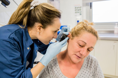 Una enfermera inspeccionando el interior de la oreja de una paciente.