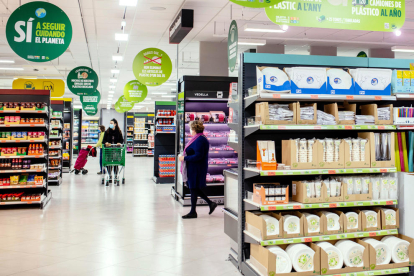 Pla general d'un supermercat de Mercadona amb clientes comprant i cartells sobre sostenibilitat el desembre del 2021. (Horitzontal)