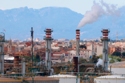 Xemeneies de la indústria química de Tarragona fumejant i, al fons, habitatges dels pobles del Morell i la Pobla de Mafumet.