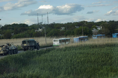 MIlitars rusos escuchan los buses que traskkades a los soldados ucranianos evacuados de la planta de Azovstal.