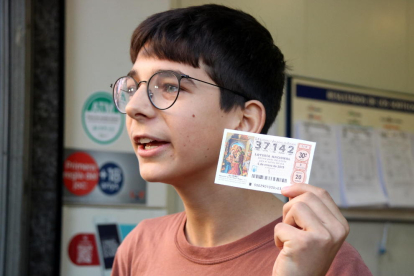 Un jove de 15 anys guanyador del primer premi del sorteig de Reis mostra una butlleta a l'administració de la Travessera de Gràcia.