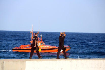 Dos agents dels Mossos d'Esquadra indicant que s'aturi el dispositiu de recerca del banyista desaparegut a la platja del Miracle de Tarragona, amb una embarcació de Salvament Marítim al fons.