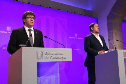 El presidente del Gobierno, Carles Puigdemont, y el vicepresidente, Oriol Junqueras, comparecen en la sala de prensa del Palau de la Generalitat para explicar los cambios en el ejecutivo.
