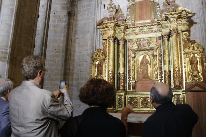 Plano medio del retablo barroco con el alcalde de Tortosa, Ferran Bel, de espalda, haciendo una foto con el móvil, y el obispo de Tortosa, Enric Benavent, de espalda, explicando las particularidades de la pieza de arte.