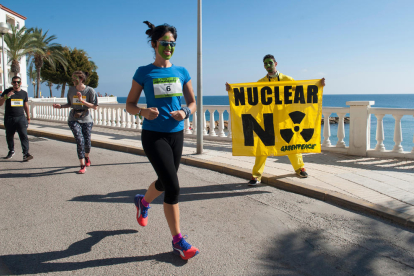 Una noia corre amb la cara pintada durant la cursa a l'Ametlla de Mar mentre un noi sosté una pancarta en contra de les nuclears