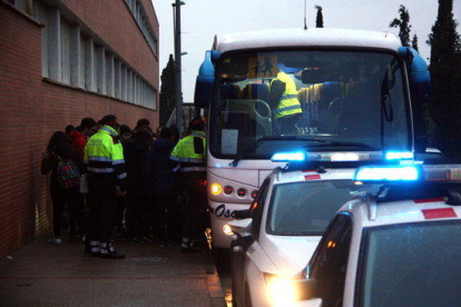 Un grup d'escolar baixant de l'autocar a les portes de l'IES Roquetes mentre els Mossos d'Esquadra inicien el control dels vehicles.