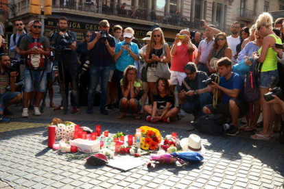 Plano general de un grupo de gente mirando las flores y las velas depositadas en homenaje a las víctimas del atentado el 18 de agosto de 2017.