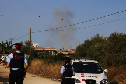Dos agentes de los Mossos d'Esquadra de espalda, con una columna de humo en frente durante una detonación controlada en Alcanar.