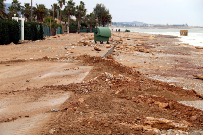 Carretera de acceso a la Platjola de les Cases d'Alcanar llena de arena y rocas mientras a los operarios lo limpian.