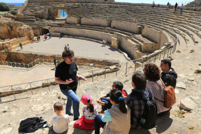 Plano abierto de varios turistas, de espalda, disfrutando de una visita guiada al anfiteatro de Tarragona.