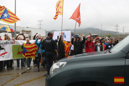 Un vehículo de la Guardia Civil marchándose de la imprenta de Sant Feliu de Llobregat mientras manifestantes independentistas exhiben esteladas y les dicen adiós con la mano.