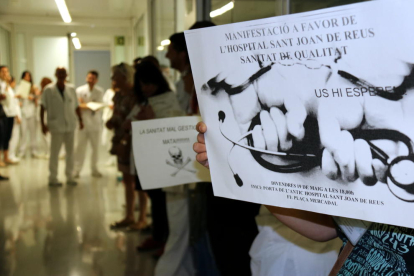 Pla detall d'una professional de l'Hospital Sant Joan de Reus, aguantant un cartell  en el qual es fa una crida a la manifestació per reivindicar els drets dels treballadors, i altres treballadors al fons, el 19 de maig del 2017