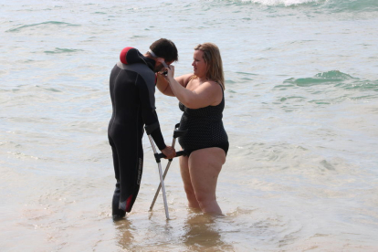 Una dona posa les ulleres de busseig a un participant que va amb crosses, dins a l'aigua. Imatge del 23 de juny de 2017