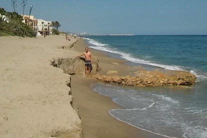 Un bañista muestra la altura del peldaño que se ha vuelto a generar con la regresión de la arena.