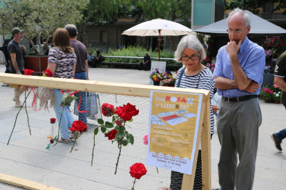 Una parella mira les flors penjades, amb un cartell que anuncia l'acció en primer pla. Imatge del 27 de maig de 2017