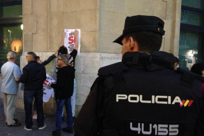Un agent de la Policia contempla com manifestants a favor del referèndum enganxen un cartell.