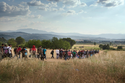 Un grupo de centenares de refugiados con hombres, mujeres y niños andando campo a través en Europa, en un plano general.