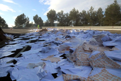Bosses de plàstic i paper escampats en un tomb de la N-240, al Coll de Lilla, entre Valls i Montblanc, on un camió ha perdut la càrrega, i un operari al fons regulant el trànsit. Imatge del 23 de novembre del 2017