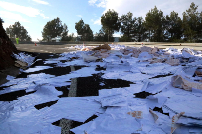 Bolsas de plástico y papel derramados en un vuelco de la N-240, en el Coll de Lilla, entre Valls y Montblanc, donde un camión ha perdido la carga, y un operario en el fondo regulando el tráfico.