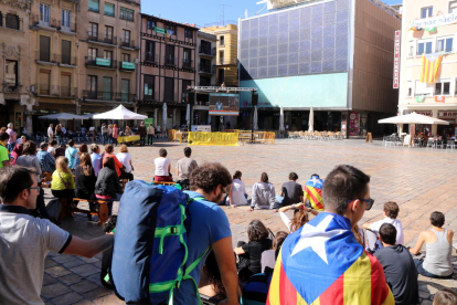 Diverses persones seguint el ple del Parlament des de la plaça del Mercadal de Reus, amb una pantalla gegant al fons.