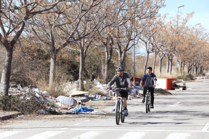 Dos veïns circulen en bicicleta per un dels carrers del polígon, completament envaït per les deixalles i la runa que s'ha abocat il·legalment.