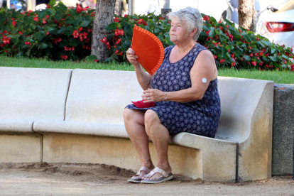Una dona fent-se vent amb un ventall en una plaça pública de Figueres davant l'onada de calor.