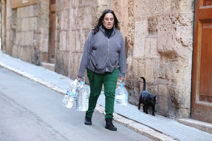 L'Elisabet carrega quatre garrafes plenes d'aigua mentre camina fins a casa seva.