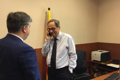 Imagen general del candidato a la investidura, Quim Torra, hablando por teléfono con Carles Puigdemont, bajo la mirada de Albert Batet de espaldas.