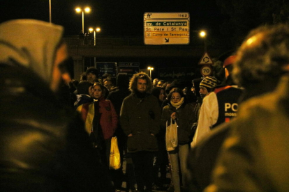 En primer pla, dos conductors d'esquenes esperant. En segon pla, enfocats, els manifestants davant de la policia, al tall de l'A-7 a Tarragona. Imatge del 24 de març de 2018